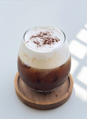 Iced Coffee with Cream Foam on White Table with Window Shadow