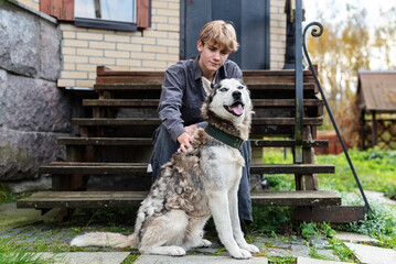 Young caucasian male with husky sitting on wooden steps outside a brick house © Rodica
