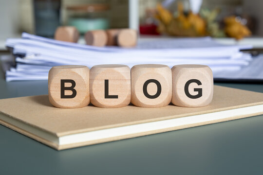 Wooden cubes spelling BLOG on a notebook with stacked documents, symbolising content creation. - Powered by Adobe
