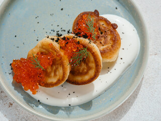 Pancakes served with red caviar. Delicious pancakes on sour cream on blue plate decorated natural red caviar of fish. Close up. Top view or flat lay