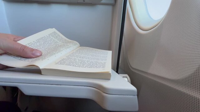 Lesemoment am Flugzeugfenster &ndash; Buch auf Klapptisch, entspanntes lesen &uuml;ber den Wolken
