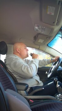 Drunk driving. The driver of the car is drinking a strong alcoholic beverage while driving. The driver drinks strong alcohol while driving - vertical video.