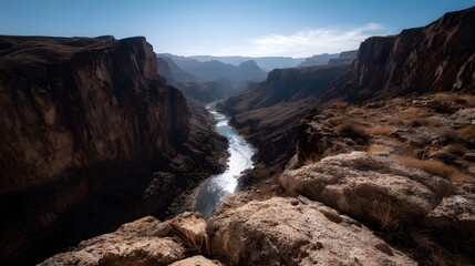 Obraz premium A sweeping vista of a grand canyon carved by a winding river with towering rugged cliffs under a clear blue sky