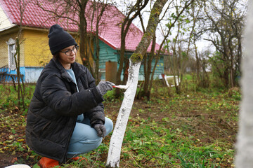 a girl is whitewashing trees	