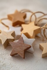 A close-up of rustic wooden and painted paper star-shaped Christmas ornaments arranged on a textured surface with natural jute twine loops for hanging