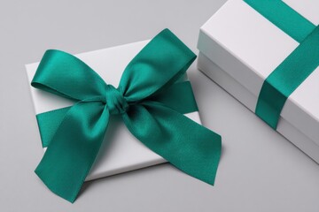 A gift box wrapped with a rich emerald green satin ribbon sits on a smooth silver background highlighting the elegance and simplicity of festive packaging