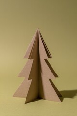 A small stylized Christmas tree constructed from folded recycled cardboard stands alone against a soft yellow background in a clean and minimal holiday presentation
