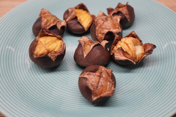 A serving of freshly roasted chestnuts with burst shells on a light blue ceramic plate, a popular autumn and winter snack