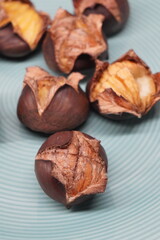 A close-up view of freshly roasted chestnuts with their shells cracked open, revealing the warm, delicious fruit inside, served on a light blue patterned plate, ready for a comforting autumn snack