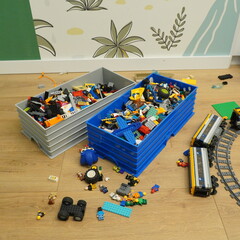 Obraz premium Messy playroom floor with blue and grey bins full of colorful LEGO building blocks and a toy train