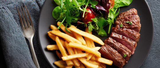 Grilled steak served with crispy fries and fresh green salad on a modern plate.