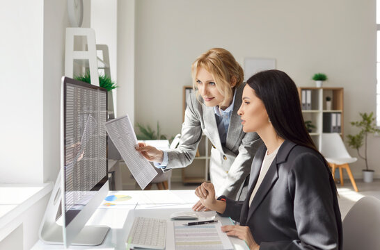 Portrait of young confident business women employees sitting at the desk on workplace, looking at pc computer monitor screen discussing company finance data in office. Accounting job concept. - Powered by Adobe