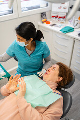 Patient expressing anxiety at dental clinic during check-up with dentist performing oral examination