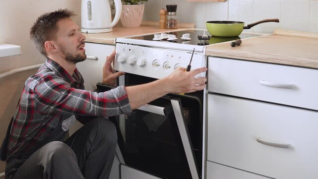 Professional appliance repair technician disassembles electric stove and carefully removes control panel before repairing it. Diagnostics and troubleshooting of complex appliances.