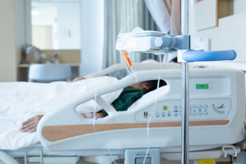 Close up set iv fluid intravenous drop saline drip in hospital room with blurry patient woman on hospital bed.Medical treatment emergency patient.Caregiver and hopeful concept.