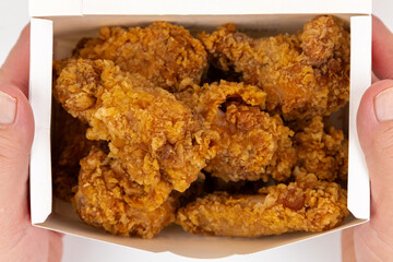 Crispy fried chicken being held in a takeout box with golden coating and juicy texture, perfect for a comforting meal at home or on the go