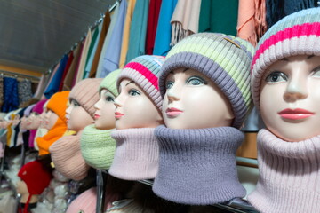 Display of colorful winter hats and scarves on mannequins in a local market showcasing a range of cozy accessories for cold weather