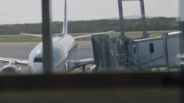 Jet bridge or jetway connecting to commercial airplane at an airport gate. Flight arriving at passenger terminal. Bridge operation moving closer to plane before disembarking or boarding jet during day