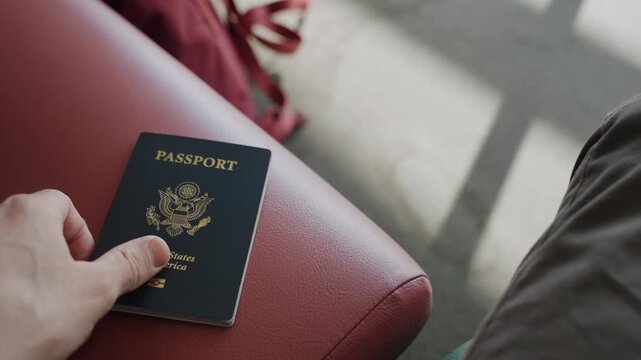 Hand rests on passport beside red leather seat. Shadowed floor, suitcase nearby. Person seems calm, waiting or preparing to travel. Ideal for travel, transit, or journey themes