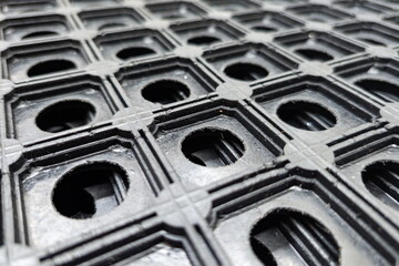 Detailed close-up view of a textured black rubber mat with holes, showcasing its design and structure in a well-lit indoor setting