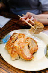 Person holding pan-fried dumpling with chopsticks from plate