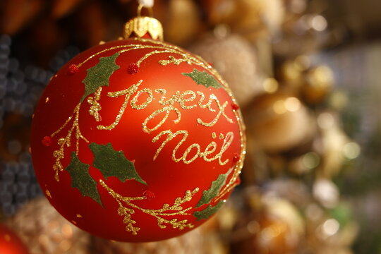 Boule de no&euml;l de couleur rouge et or ronde portant l'inscription joyeux no&euml;l et des incrustations de feuilles vertes