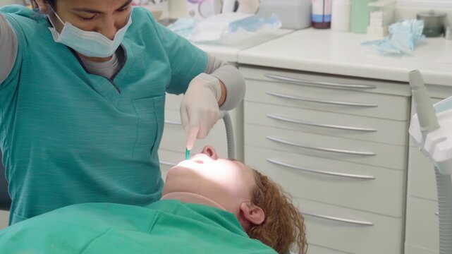 Experienced woman dentist at a clinic performing a dental procedure on a patient's teeth with the help of a dental drill and suction device