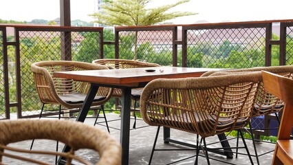 Obraz premium Outdoor cafe seating area on a balcony with rattan chairs and a modern wooden table