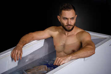Young man taking an ice bath among ice cubes. Сryotherapy and recovery. Selective focus.