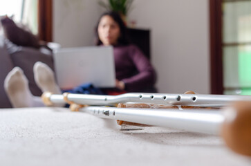 Crunch foreground photo with a young disabled woman using her laptop laying on the couch on background.