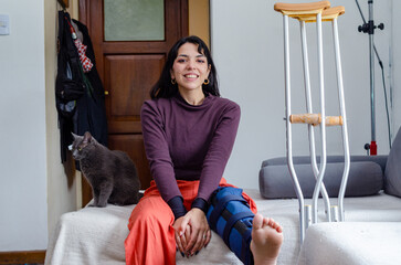 Portrait of a smiling young woman with a broken leg sitting on a couch.