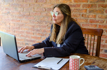 Mature woman working with a laptop.Woman taking notes while talking on mobile phone.