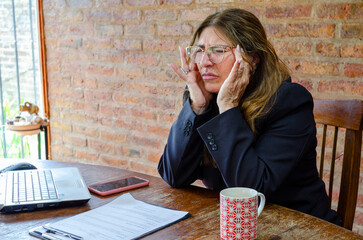 Mature female employee working from home feeling headache.