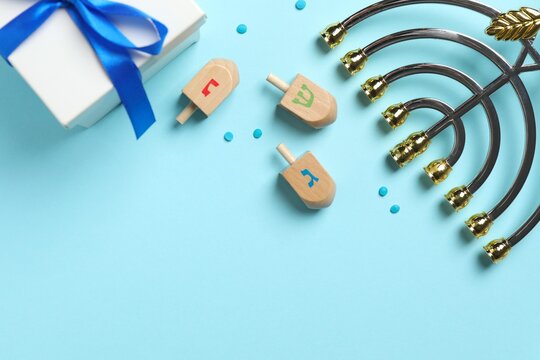 Hanukkah celebration flat lay composition with golden menorah, gift box and dreidel set. Happy Hanukkah greeting card with Jewish decor on blue table