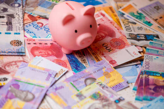A pink piggy bank sits amidst a vibrant, scattered pile of various international banknotes, prominently featuring Angolan Kwanza notes, symbolizing global savings, diverse wealth, and foreign exchange
