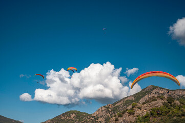 Oludeniz, Turkey. A man on a colorful paraglider flies against a backdrop of cloudy skies and...