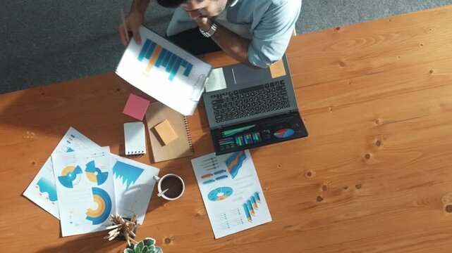 Top aerial view of manager working on laptop while looking at data analysis. Leader compare financial statistic graph while making decision at meeting table with document scatter around. Convocation.
