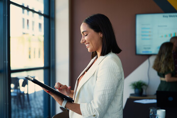 Side view of smiling young businesswoman in smart casual using tablet in office during daytime