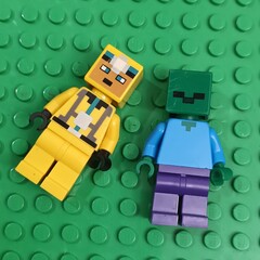 Fototapeta premium Two Minecraft Lego Minifigures, a Bee and a Zombie, against a green background of Lego bricks