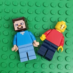 Fototapeta premium Two LEGO minifigures, the character Steve from the popular video game Minecraft and a classic figure, lying on a green baseplate