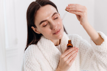 Woman applying skincare serum during morning routine in modern bathroom