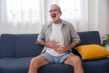 Elderly man suffering from severe chest or stomach pain while sitting at home, showing signs of heart attack, gastric issue, or abdominal emergency. Ideal for health and medical use.