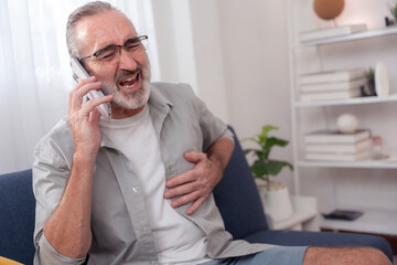 Elderly man experiencing chest pain while using smartphone at home, symbolizing heart attack...