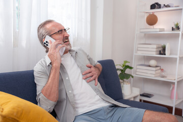 Elderly man experiencing chest pain while using smartphone at home, symbolizing heart attack...