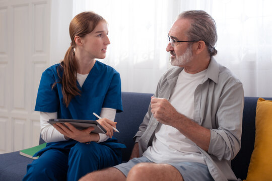 Elderly man receiving medication advice from a nurse at home. Concept of home healthcare, senior patient care, aging wellness, chronic illness management, or retirement support.