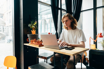 Young man working on laptop in a modern cafe setting with chess pieces displayed