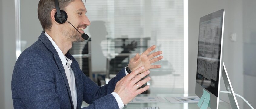 Man in headset talking during online video call, working in office, consulting remote customers, providing technical support. Business people concept