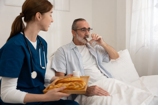 Female nurse serving breakfast and medication to senior man in bed while he drinks water. Ideal for home healthcare, elderly support, daily care routine, and medical service visuals. - Powered by Adobe