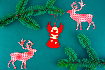 Festive Christmas background with paper angel and reindeer ornaments on dark green surface decorated with fir branches.