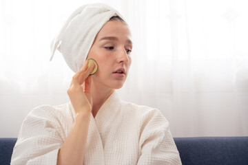 Woman with Cucumber Slices on Eyes. Relaxed woman in white bathrobe with towel on head. skincare...